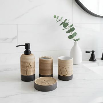A set of three wooden bathroom accessories with black bases, including a pump bottle, a tooth holder, and a cup, arranged on a white marble countertop next to a white vase with green eucalyptus stems.
