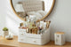 Cosmetic organizer with skincare products on a wooden desk, reflected in a round mirror.